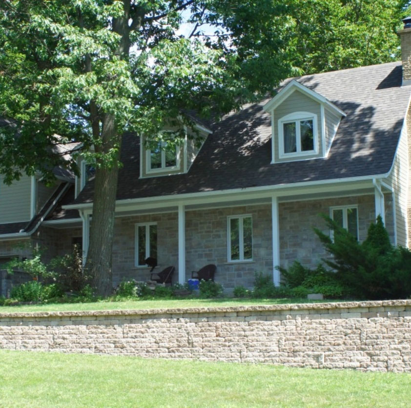 Maison en brique claire avec jardin et rénovations, illustrant le printemps et l'harmonie entre l'architecture, la nature et les travaux de rénovation réalisés par Sylca Construction.